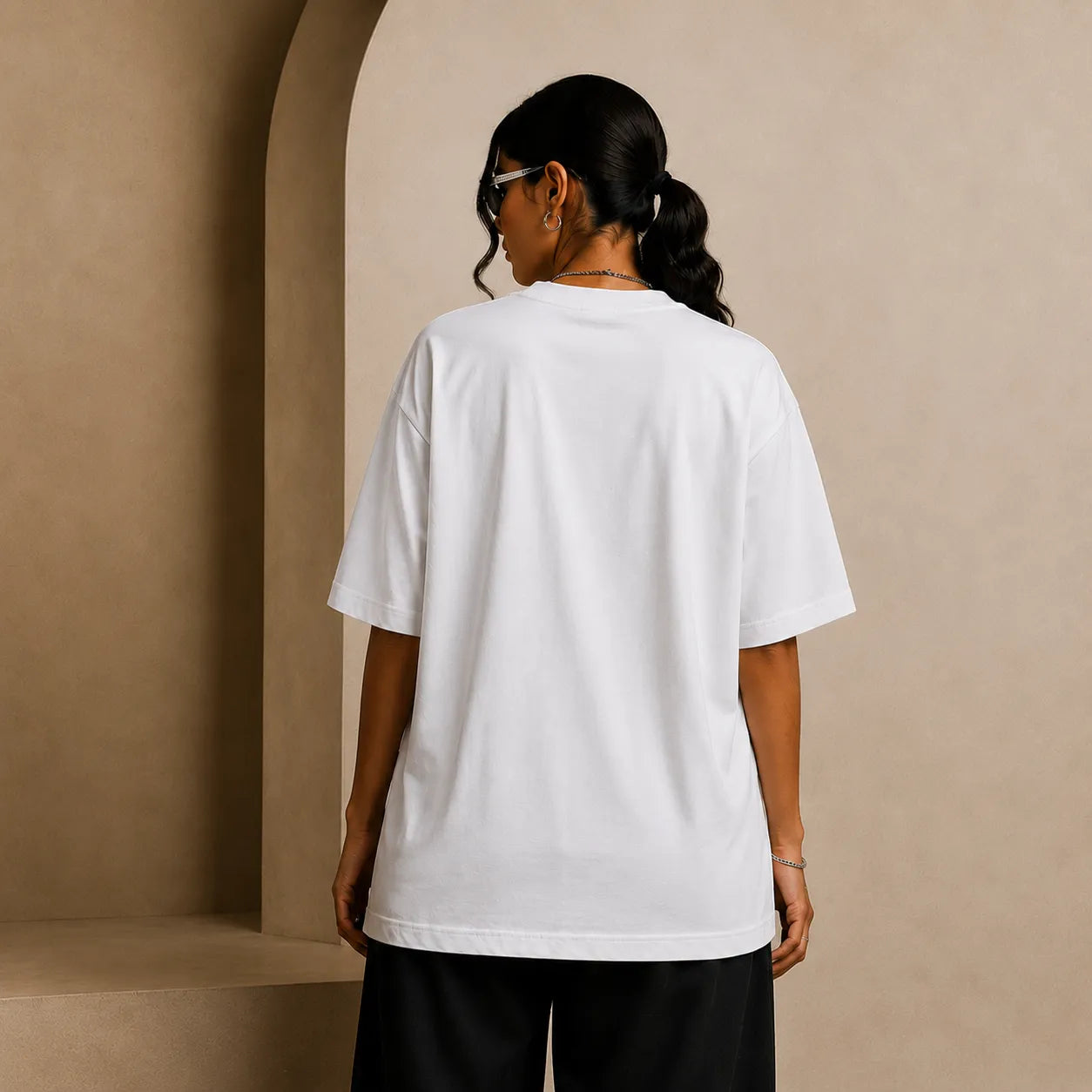 Person wearing a white t-shirt and black pants against a beige wall.